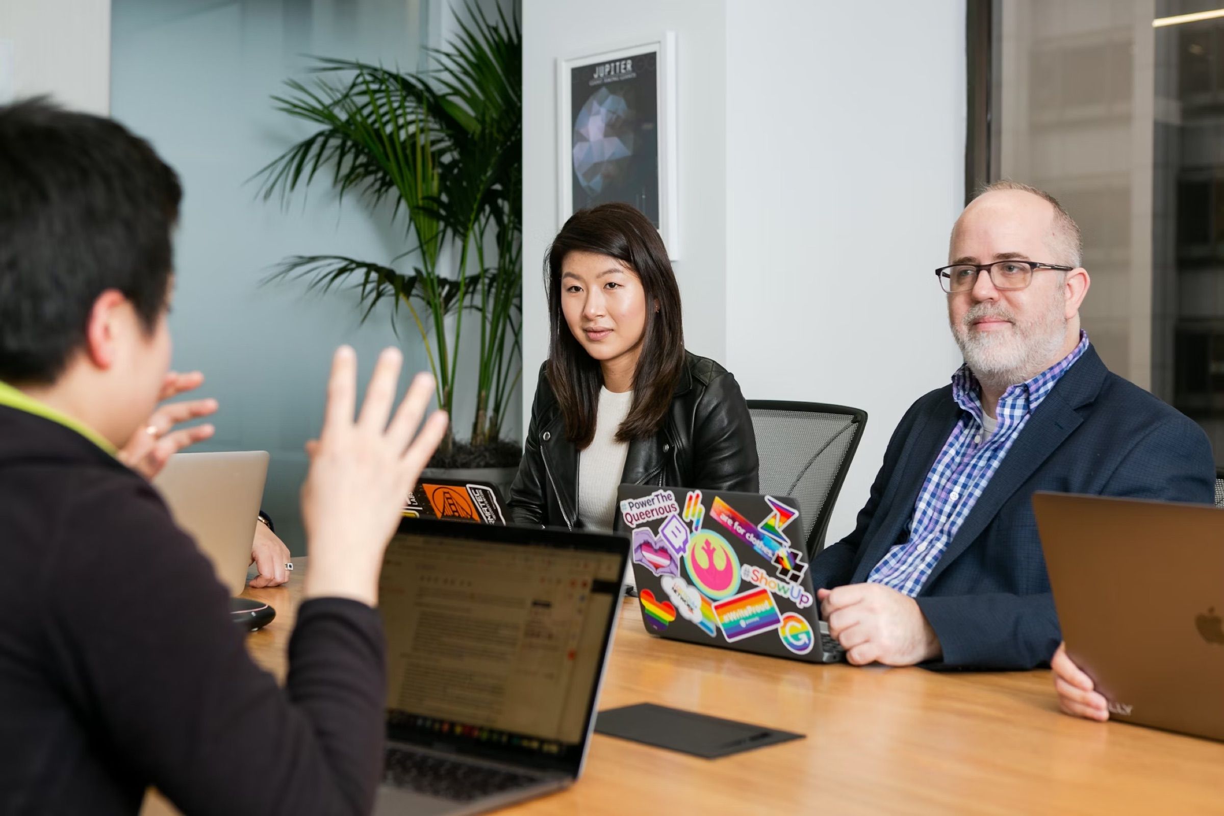 Three people talking across a meeting table with laptops
