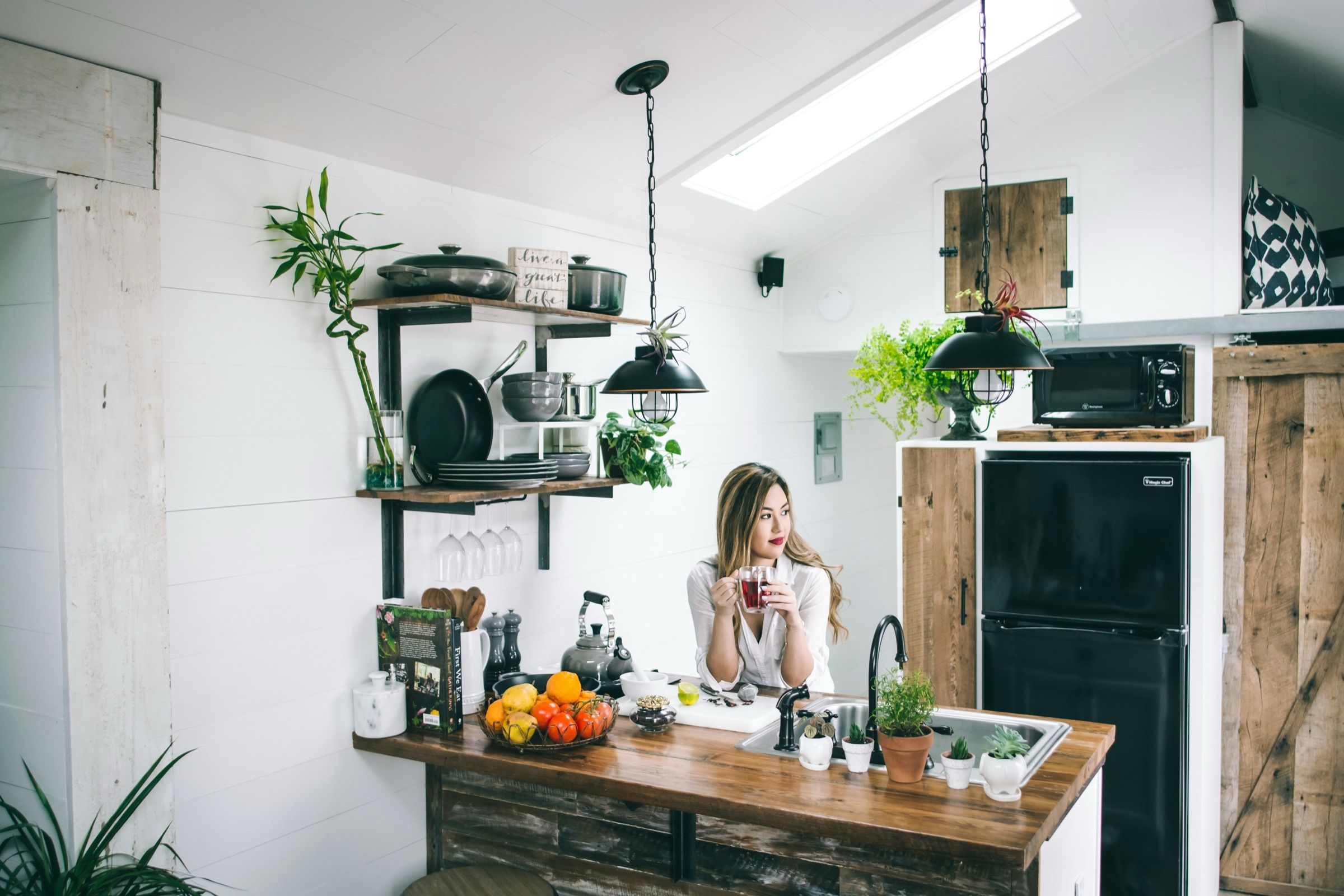 A woman drinking coffee in a bright rented kitchen with open shelves and hanging plants
