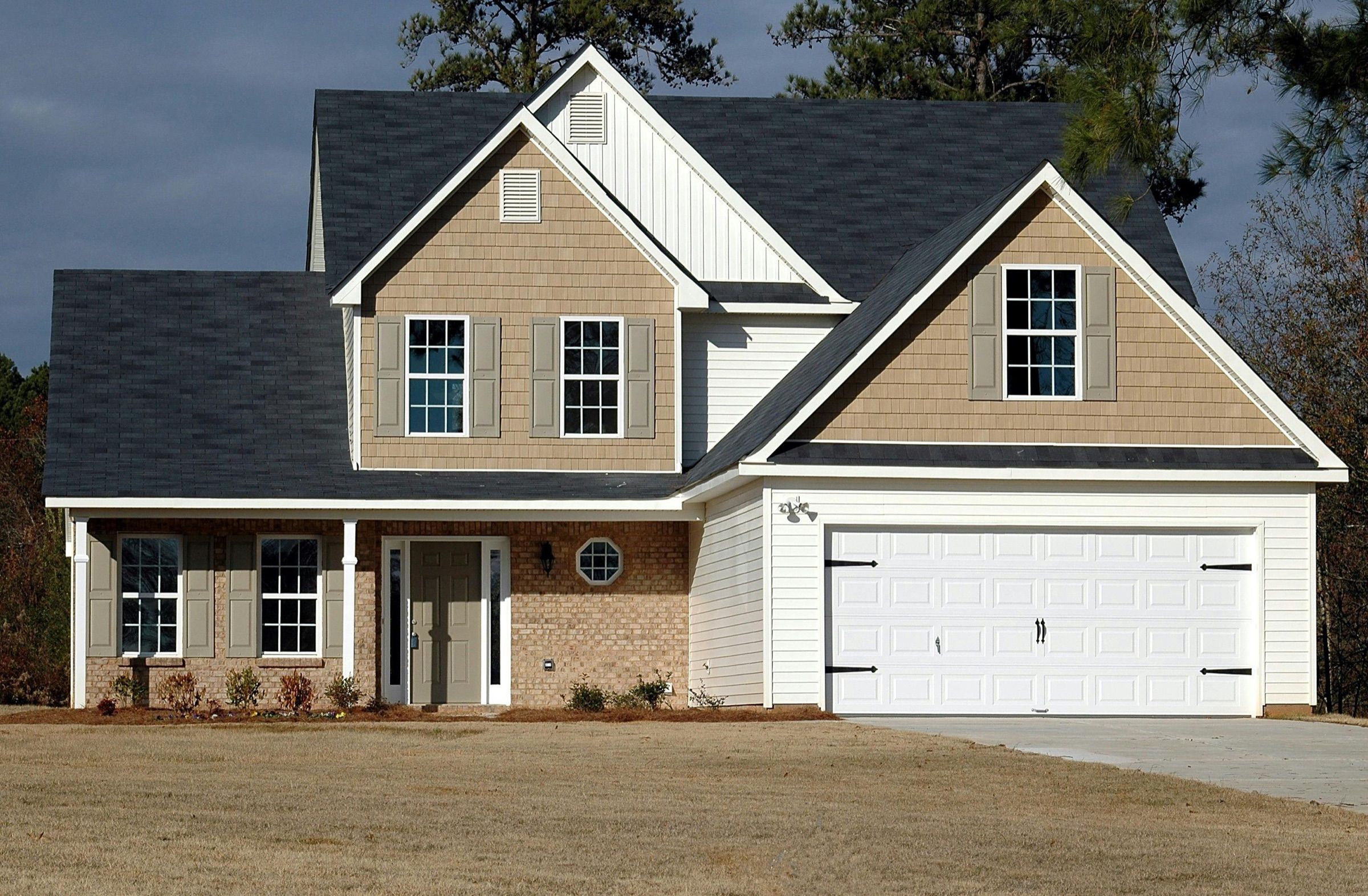 Detached gabled house with tan siding, white garage door and lawn