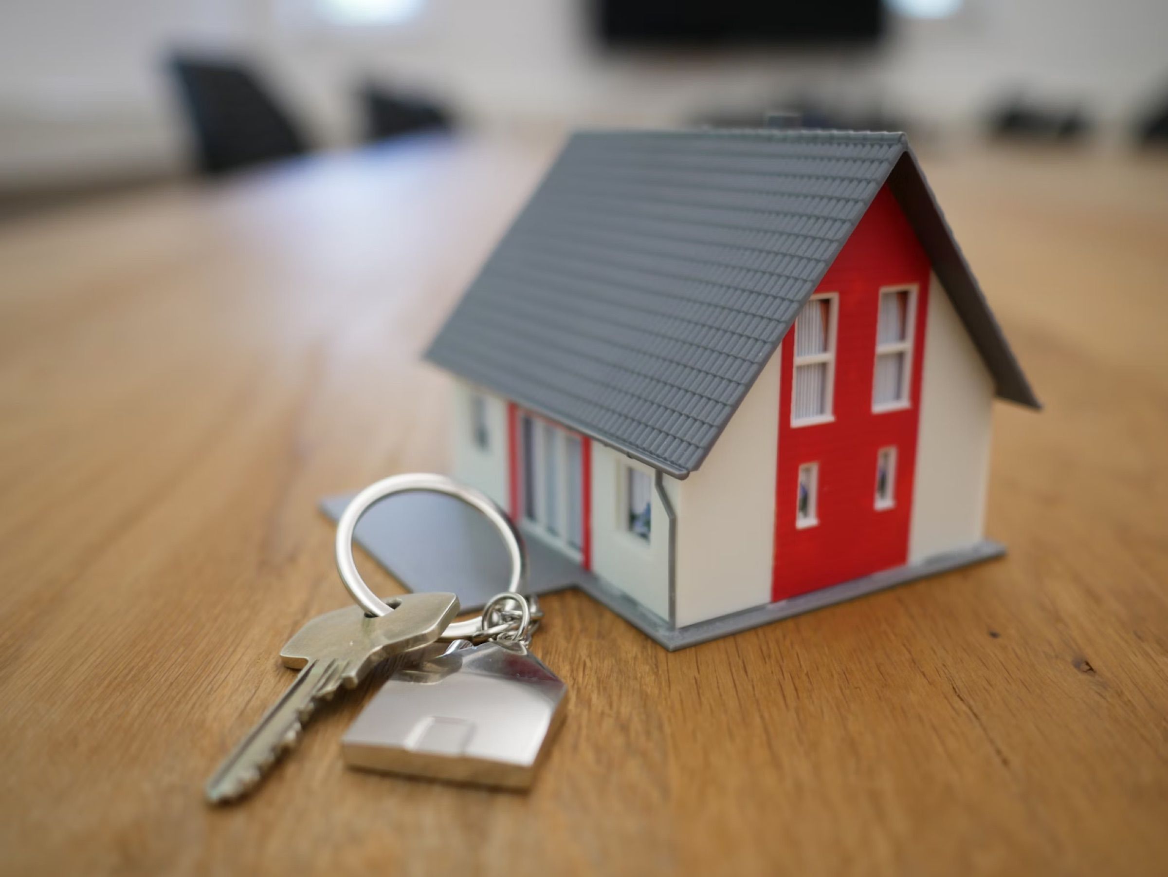 A set of house keys on a ring next to a small model house on a wooden table