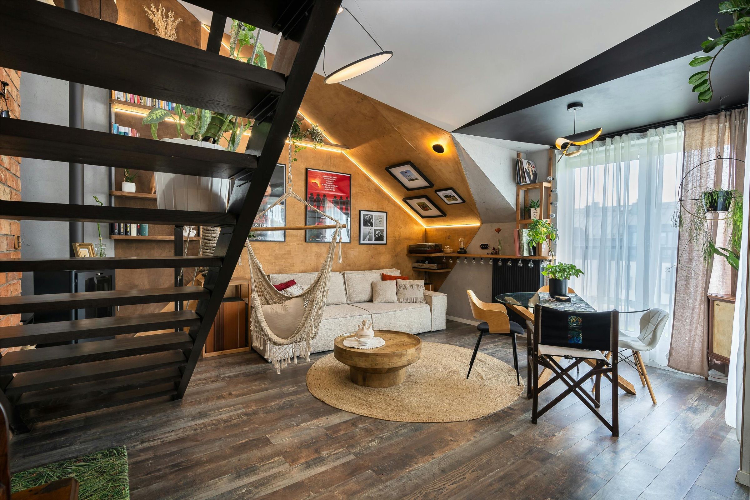 Open-plan loft living room with a black steel staircase, hammock chair and dining table