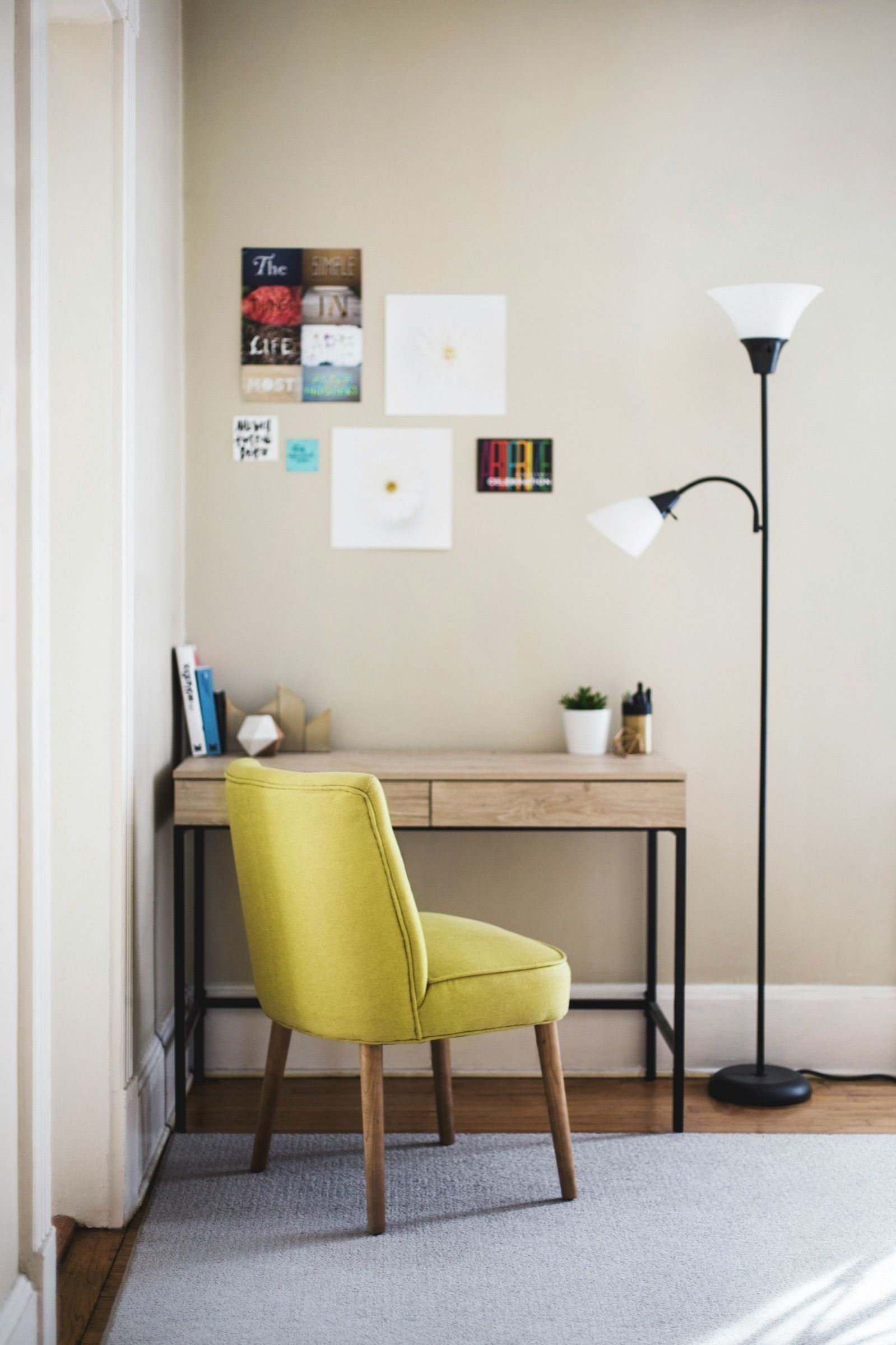 A small home office corner with a yellow chair, a wooden desk and a tall floor lamp